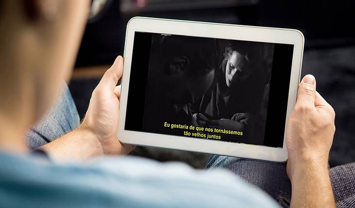 Imagem de um homem assistindo a um filme com legendas em seu Tablet